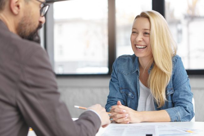 Happy blonde female manager in fashionable clothes has pleasant conversation with male colleague, discuss successful strategy for startup, chaeck list of affairs, consult new project together