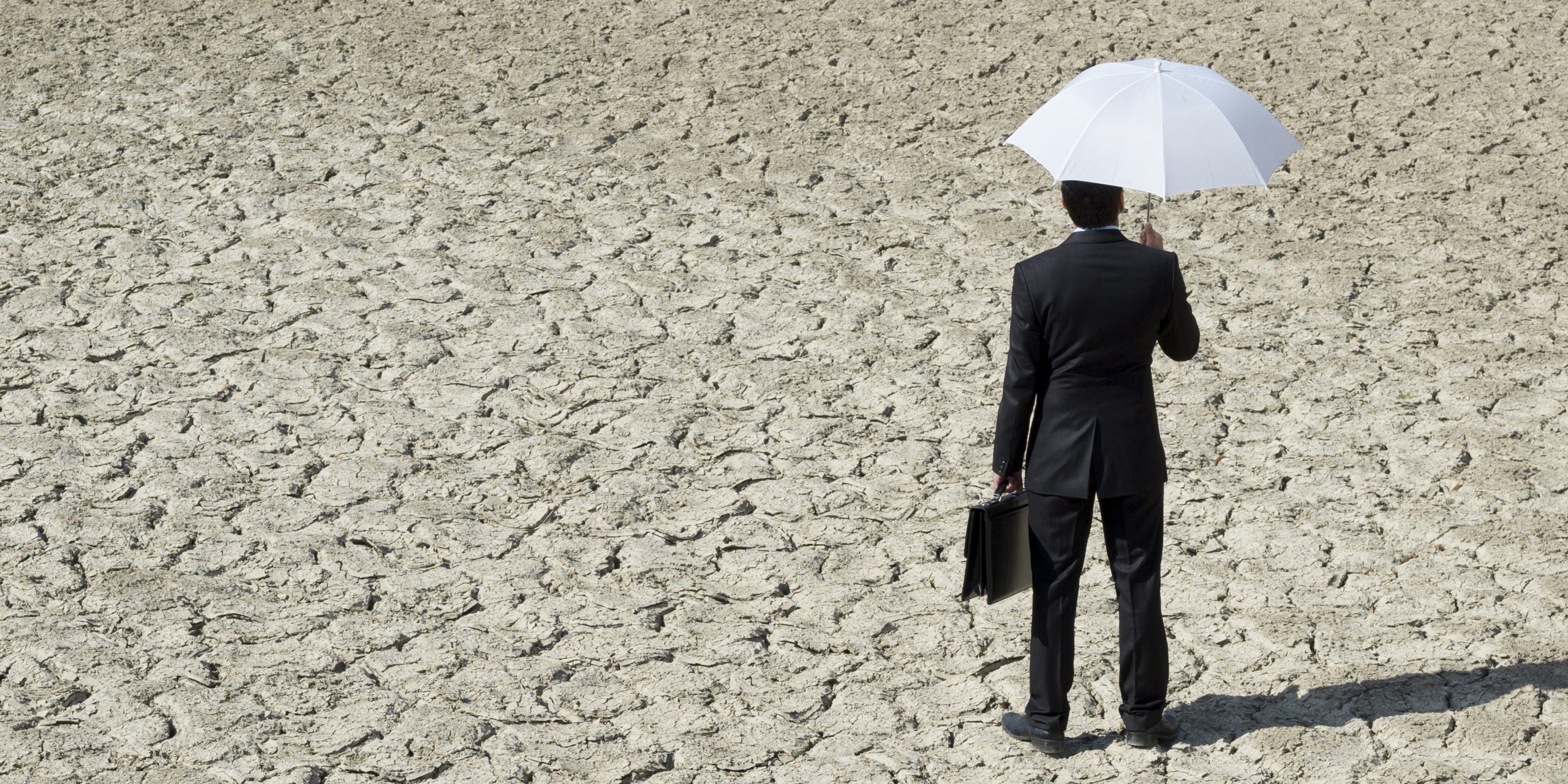 Lost businessman holding umbrella in desert